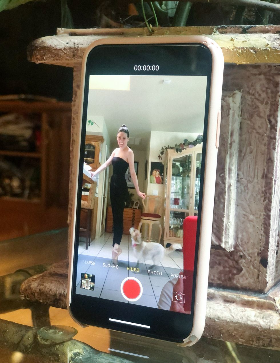Image through an iPhone video of Peck standing on pointe at her kitchen counter, with her dog Cali by her feet.
