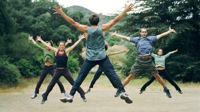A group of people all jump in the air, making an X shape with each of their bodies. 