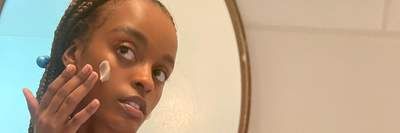 India Bradley takes a selfie via a handheld mirror while she rubs lotion into her cheek. 