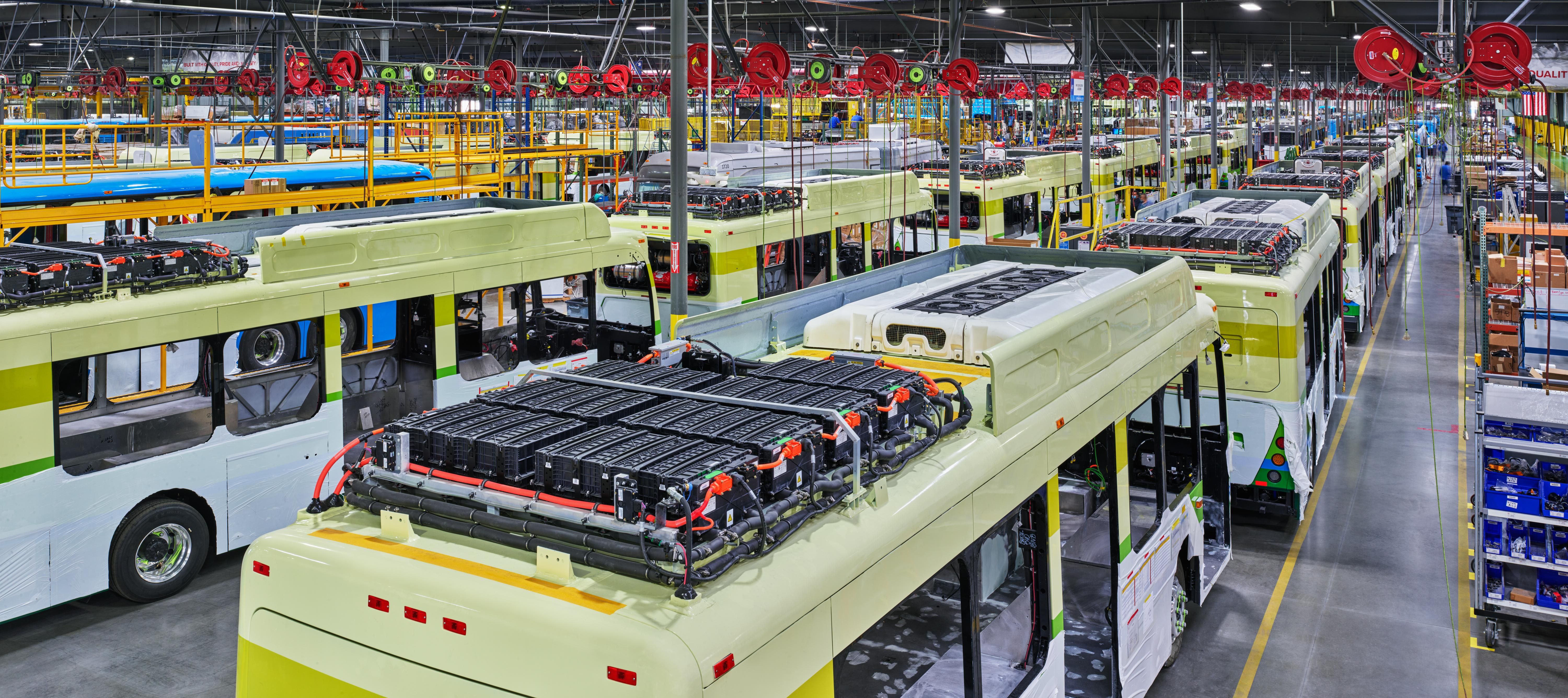 Dozens of yellow mass transit buses are shown getting the finishing touches on the factory floor.