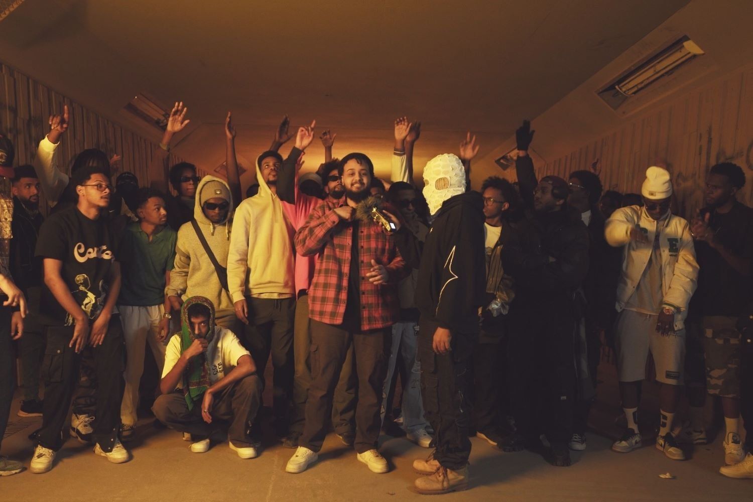 Sudanese rappers gathered in a tunnel in a secret location in Cairo, dancing and lifting their arms to the performance of a rapper in a black and red checkered shirt.