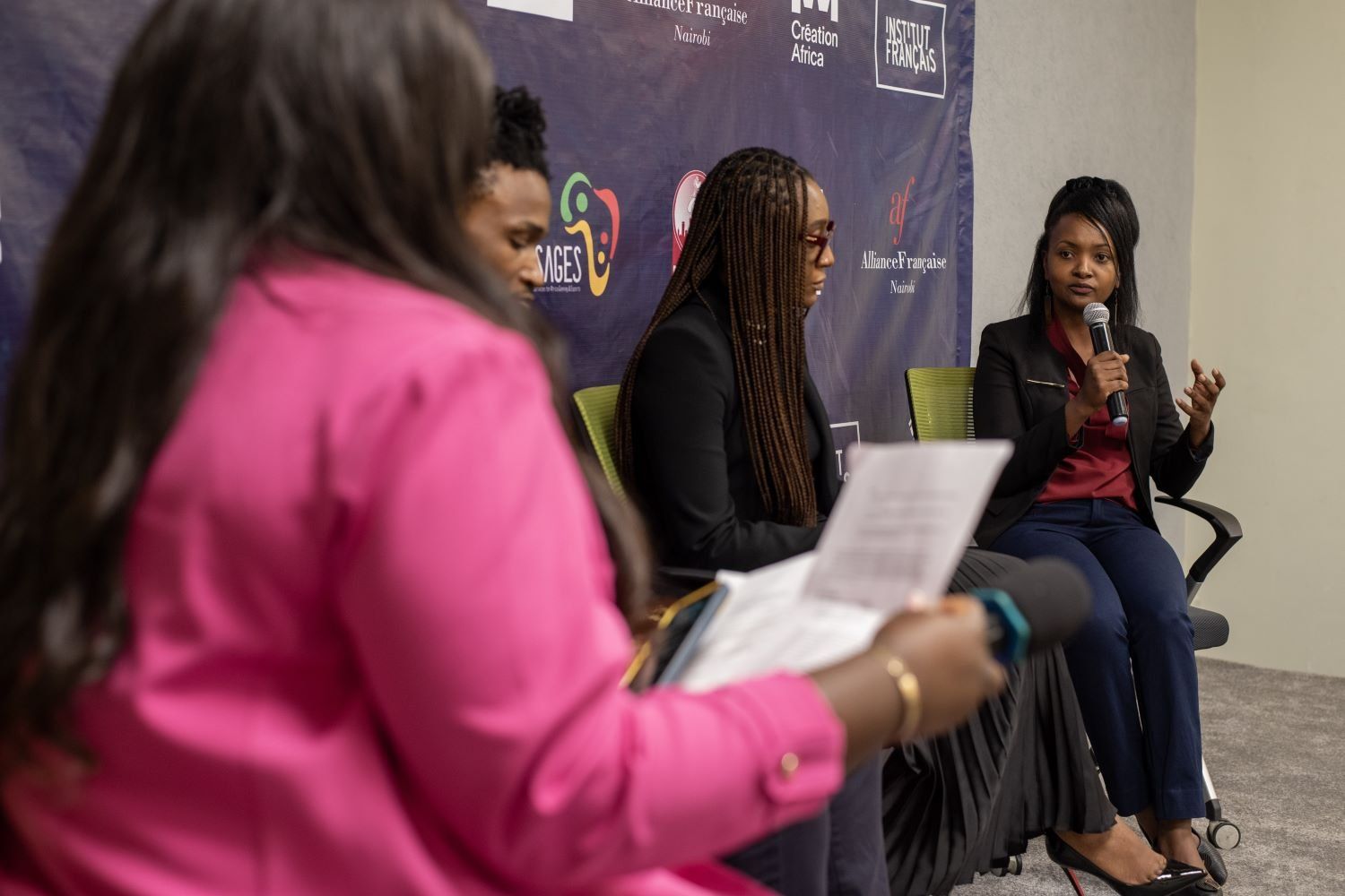 Ann Ndanu, founder of NAICCON, speaking into a microphone on a panel at a Nairobi Comic Con event, alongside other panelists.