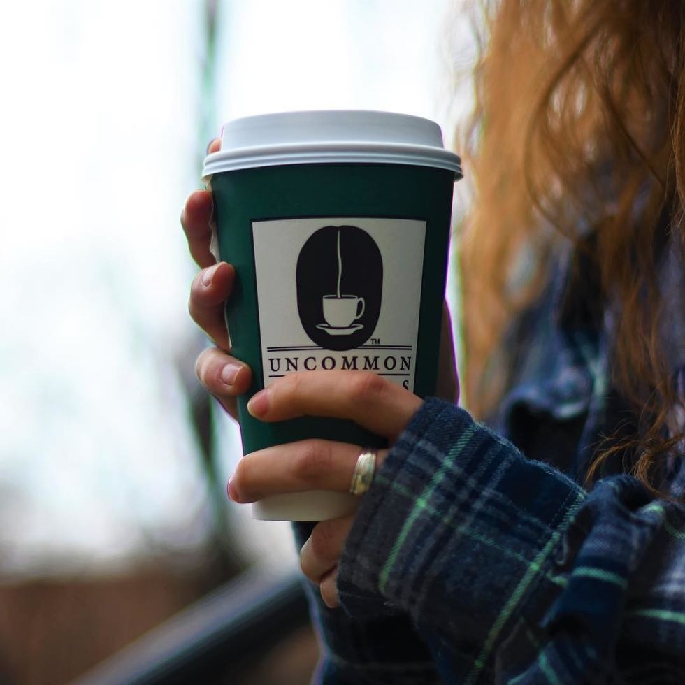 person holding cup of uncommon grounds coffee