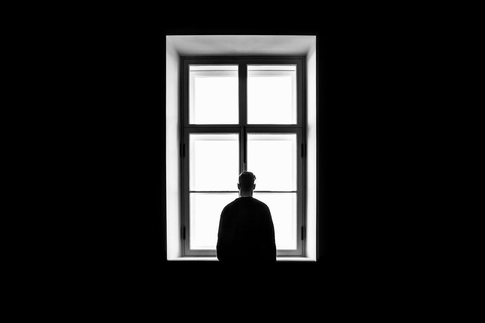 Black and white photo of a man standing next to a window