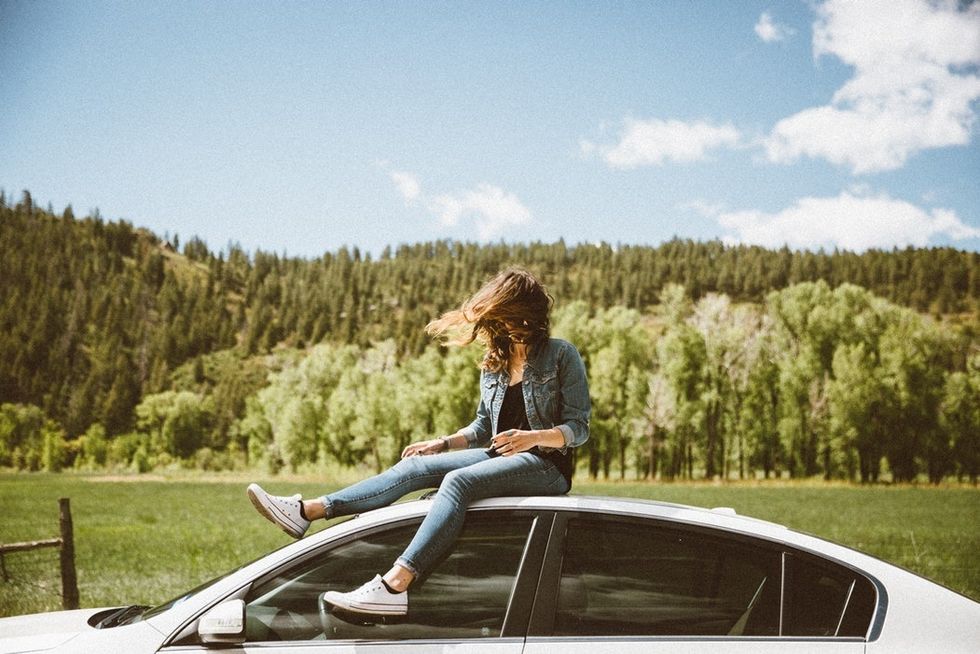 woman in jeans and denim jacket sitting on top of white car on sunny day
