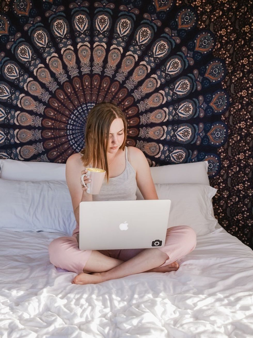 woman drinking coffee working on laptop in bed
