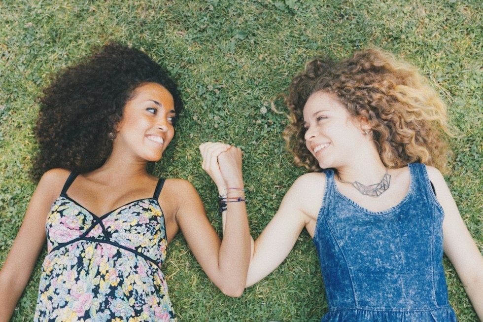 two beautiful women best friends lying together in the grass holding hands