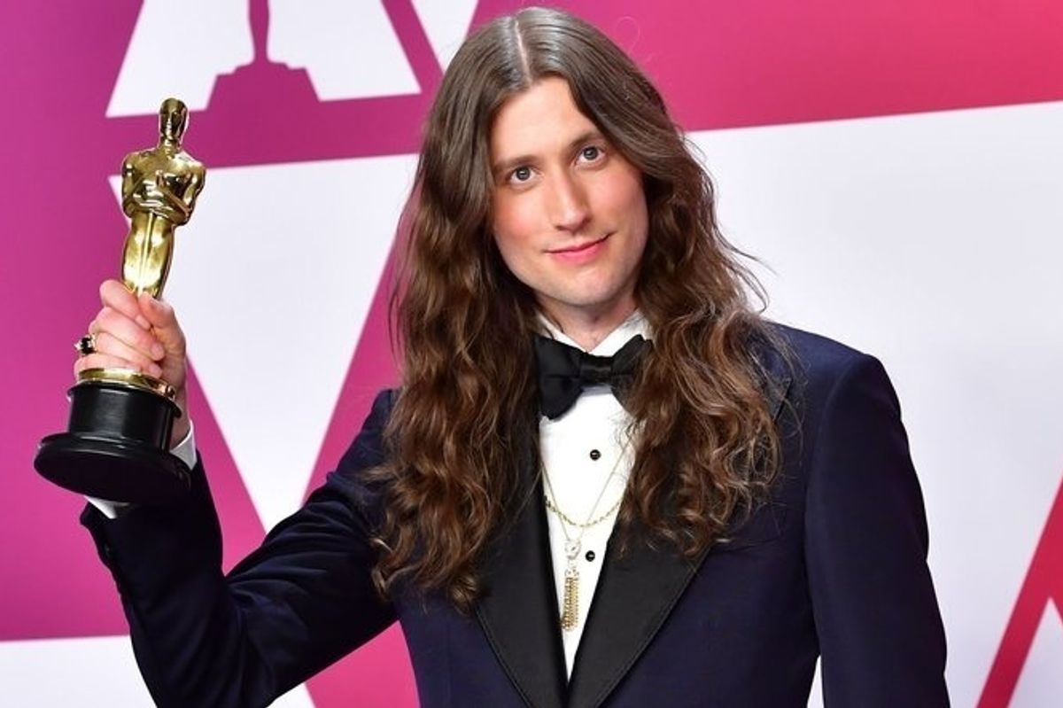 man holding Oscar in a black tux with long hair