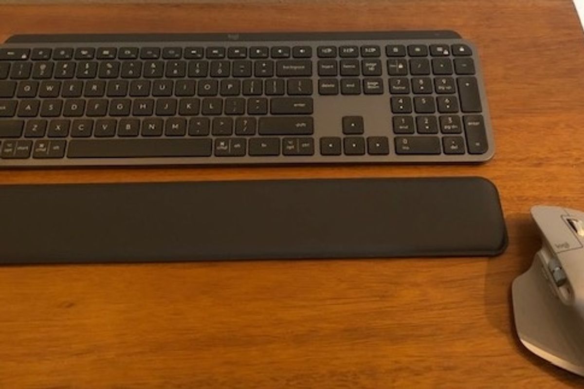 A keyboard, wrist pad, and silver mouse on a wooden table