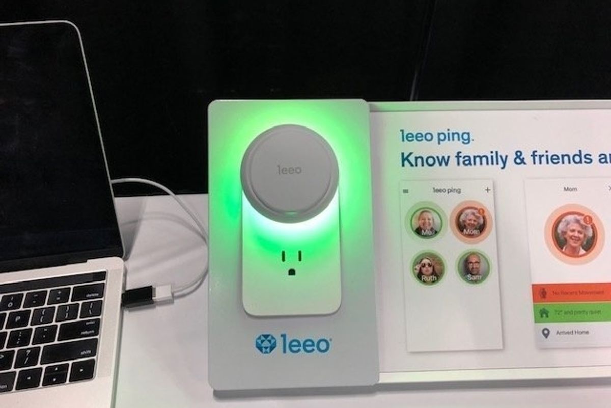 A device shining green, next to a computer on a white table with the name 'leeo' across the bottom