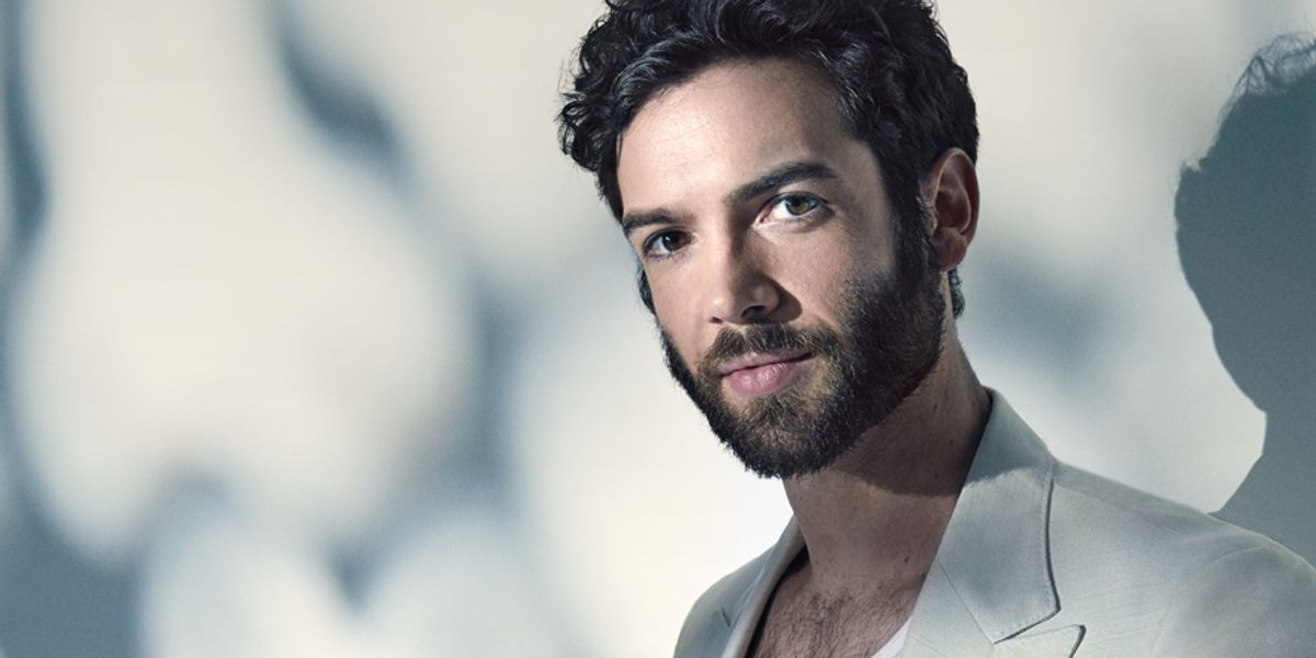 Actor Ethan Peck of Star Trek Discovery wears a white jacket and tank top against a white wall.