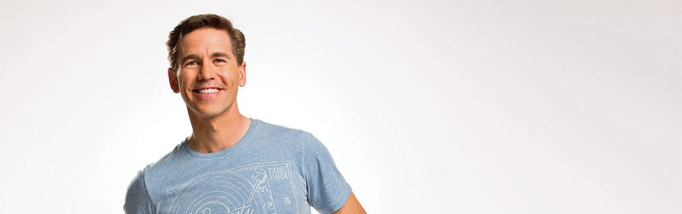 Brian Dietzen smiles for the camera in a blue tee with a record player diagram.