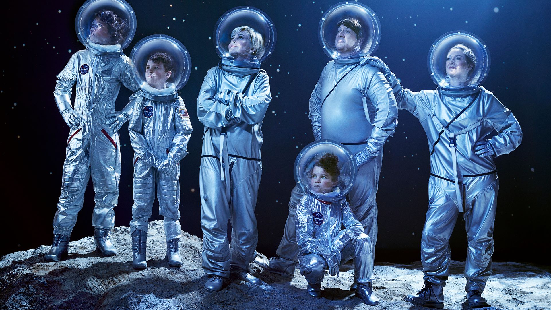 The cast of Young Sheldon wears space suits and stands on a rocky moonscape.