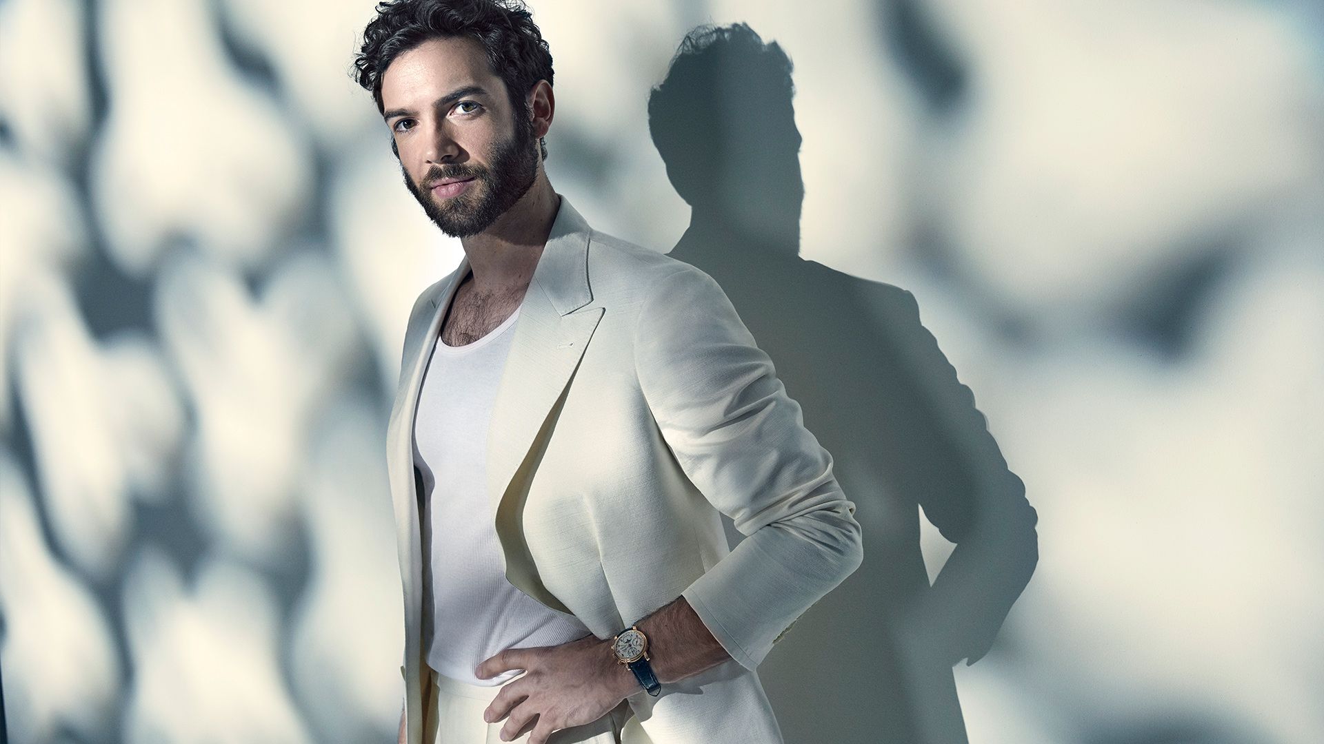 Actor Ethan Peck of Star Trek Discovery wears a white suit and white tank top against a white wall.
