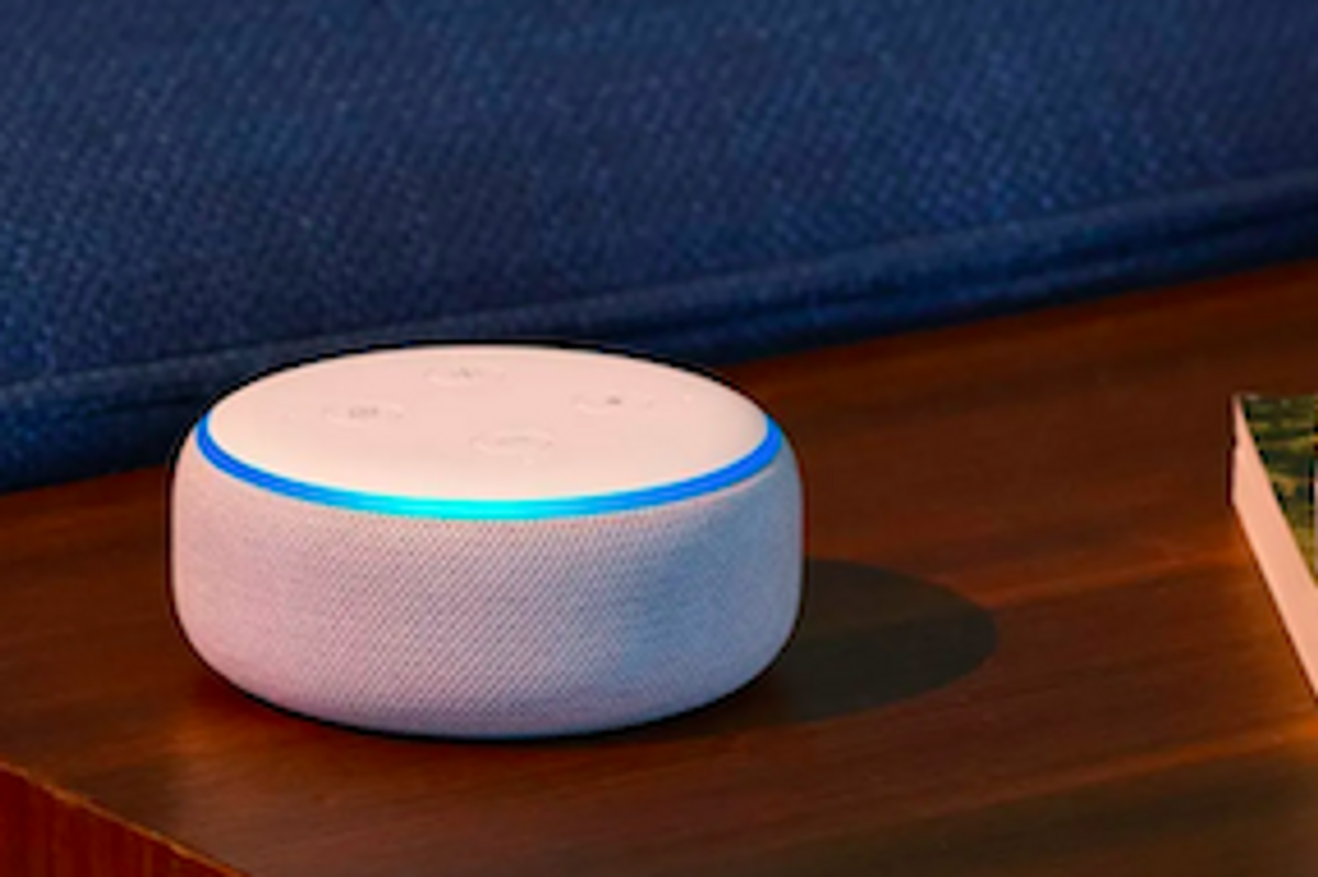 A white, fabric-covered Amazon Echo Dot on a dark wood table