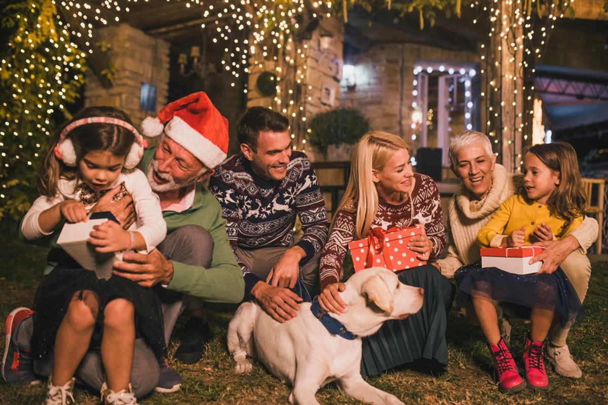 A multi-generational family opening presents outside with lights around them