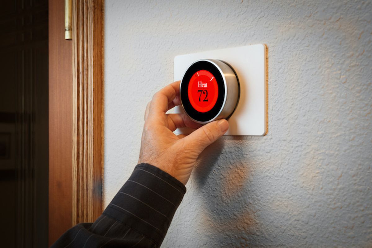 A hand adjusting a smart thermostat on a wall