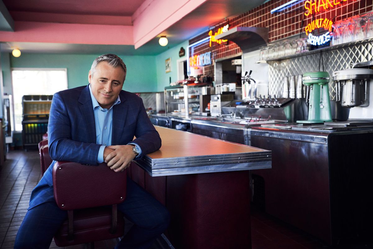 Actor Matt LeBlanc in a tailored suit, sitting at the counter of a classic 50s diner.