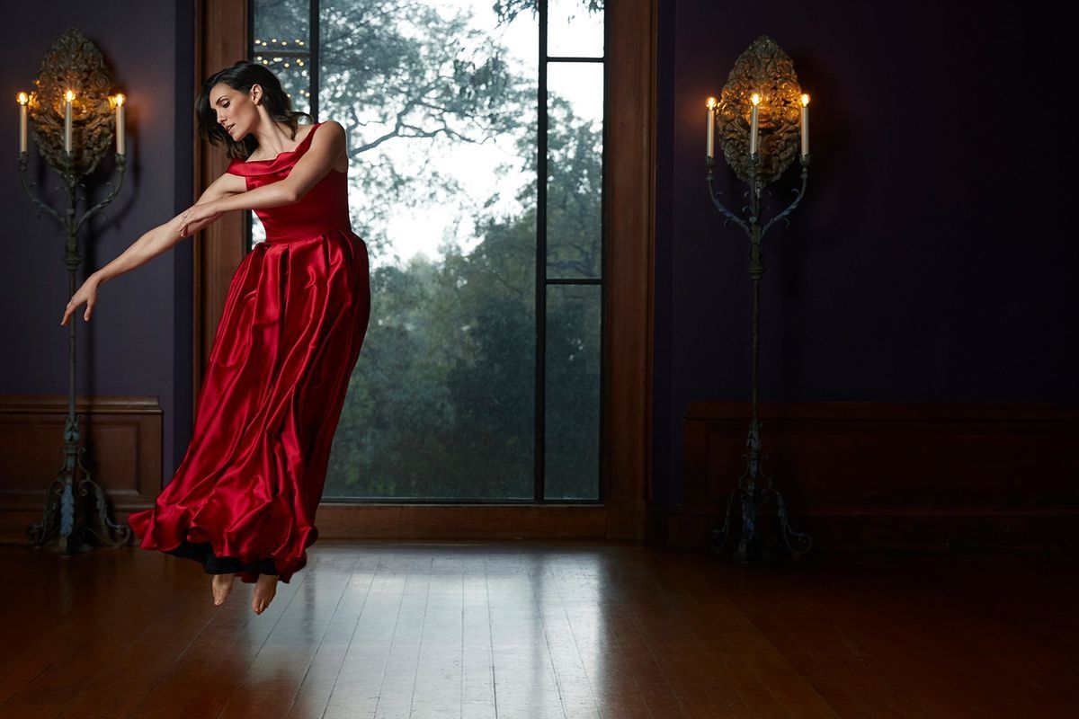 Daniela Ruah in a rich red dress leaping delicately off of the floor