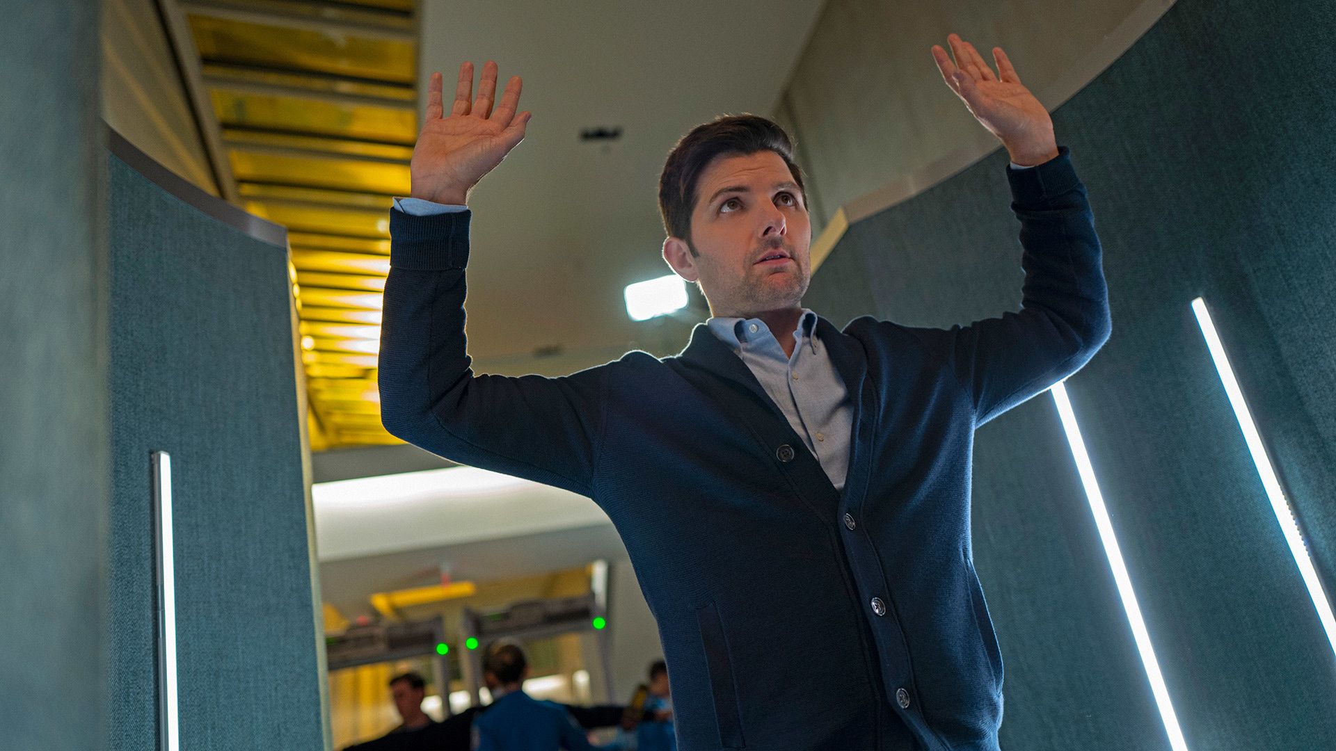 Adam Scott wears a cardigan sweater while putting his hands up prior to being arrested.