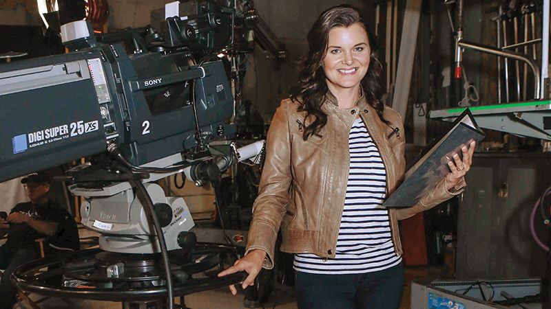 Heather Tom behind the scenes with a script and a large camera.