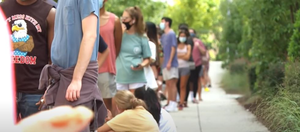 College students wait in a long line, some wearing masks. 