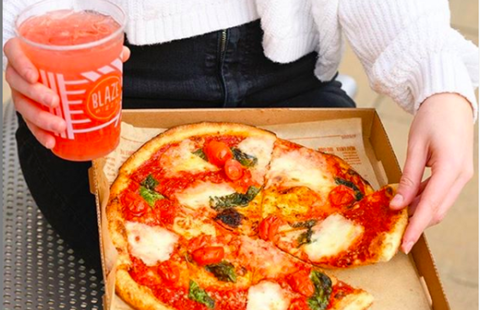 person holding pizza in their lap while holding a red drink in the other hand