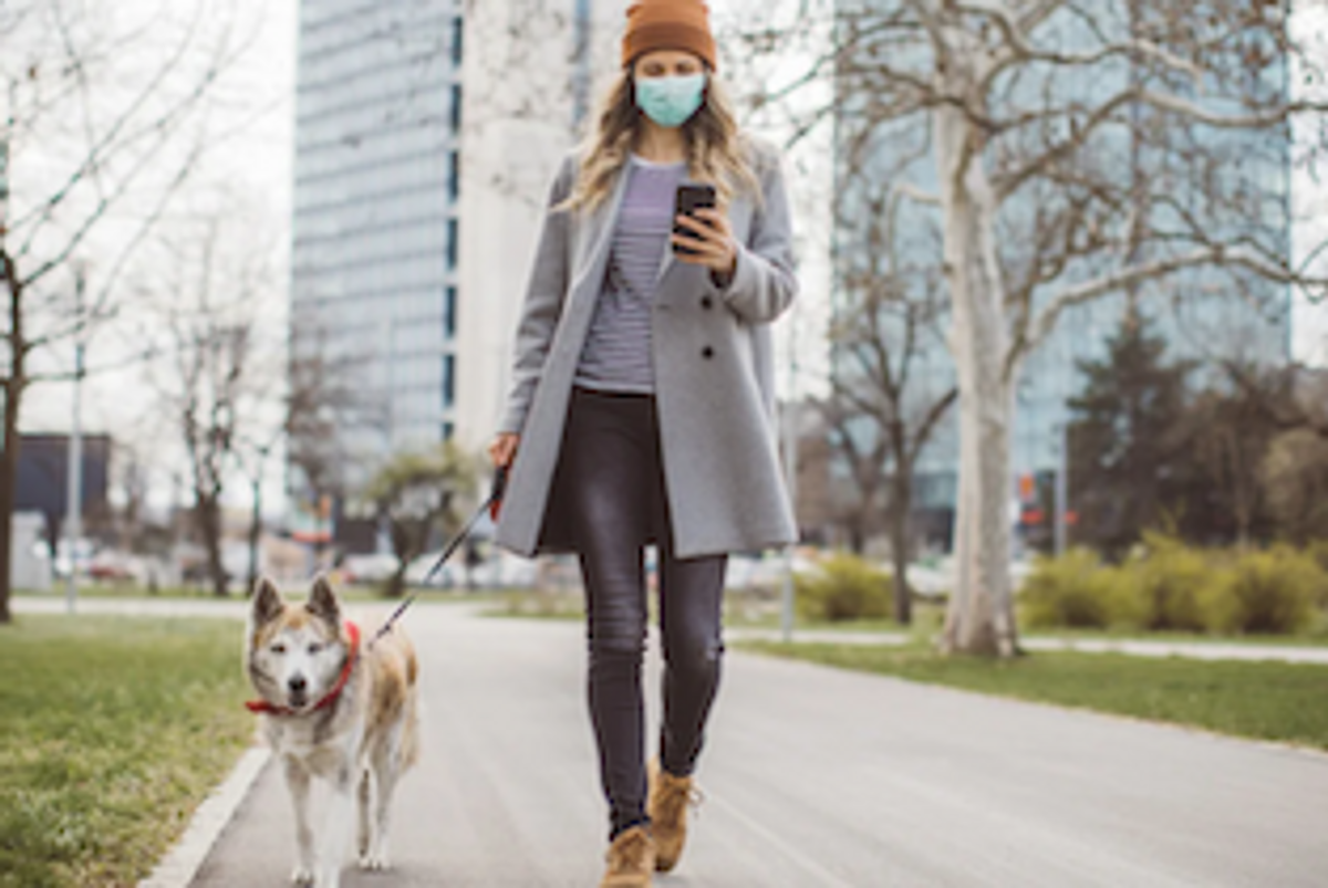 A woman walking a dog on her mobile phone with a mask