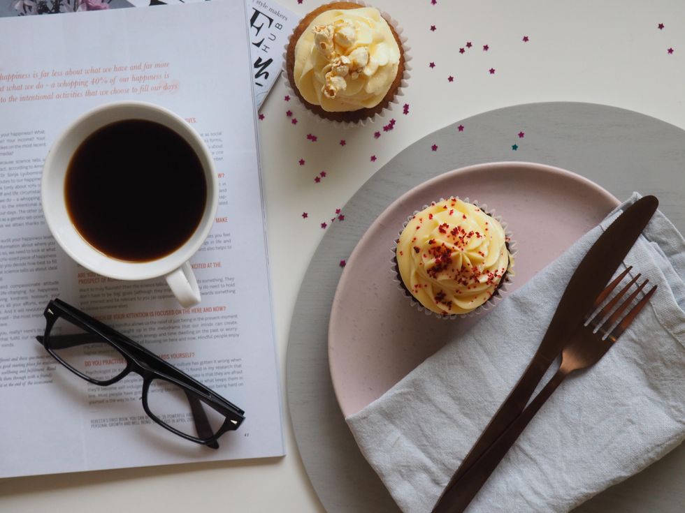 Two cupcakes with a coffee mug, plates, and glasses in the background.