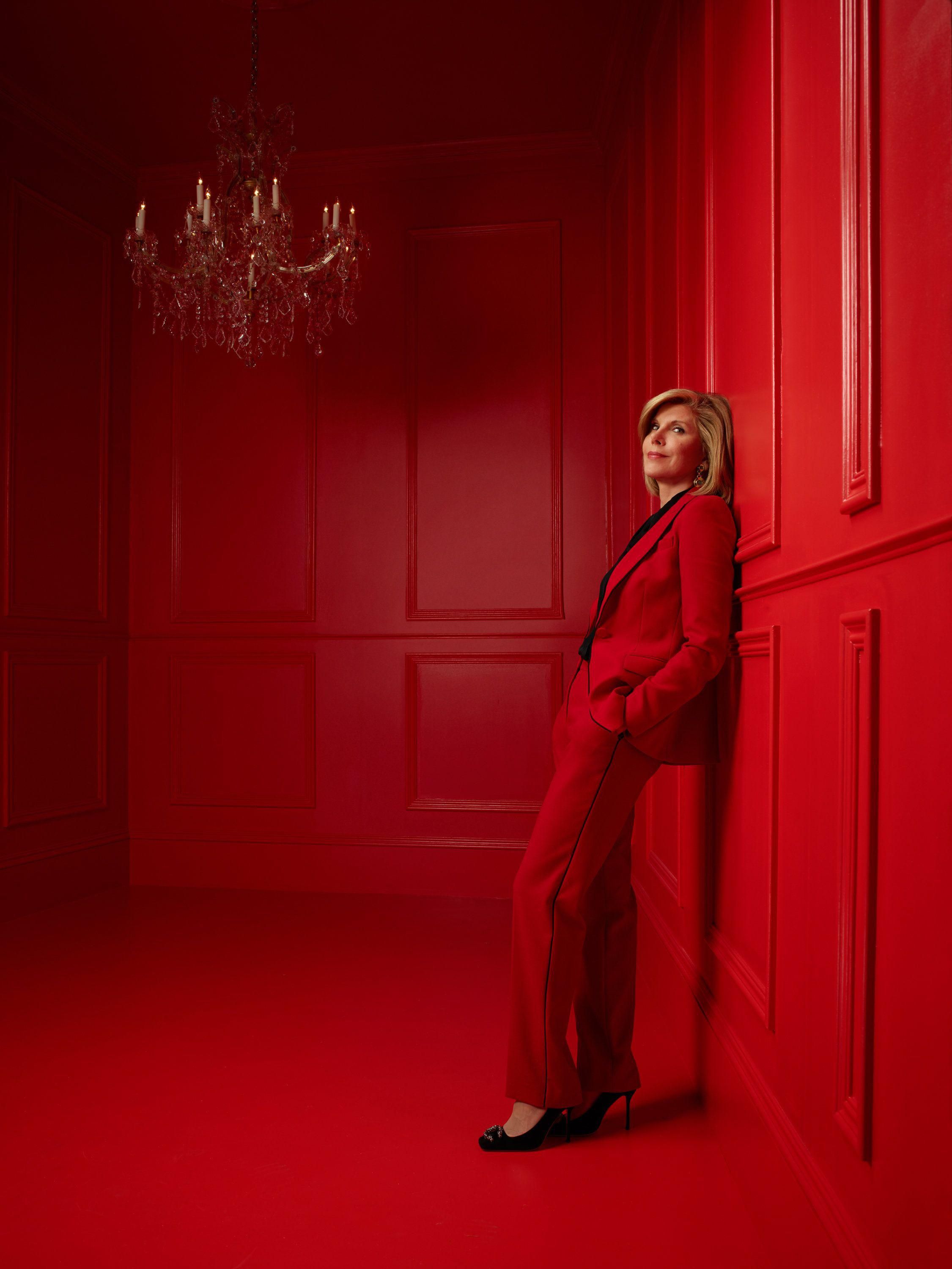 Christine Baranski wears a red suit as she leans against the wall of a matching red room