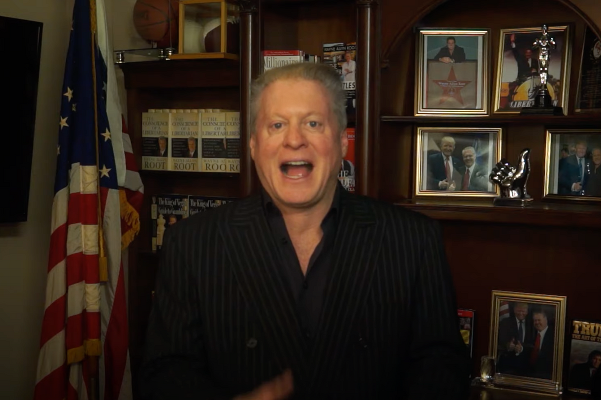 Wayne Allyn Root standing in front of a bunch of pictures of himself and Trump.