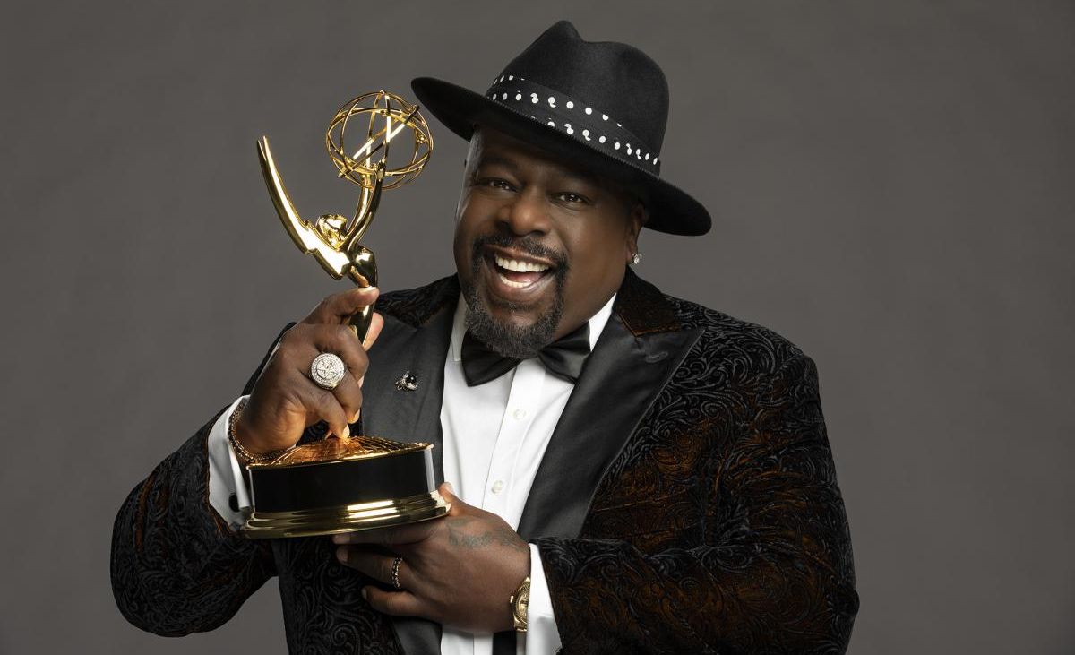 Cedric the Entertainer wearing a black fedora and holding an Emmy Award