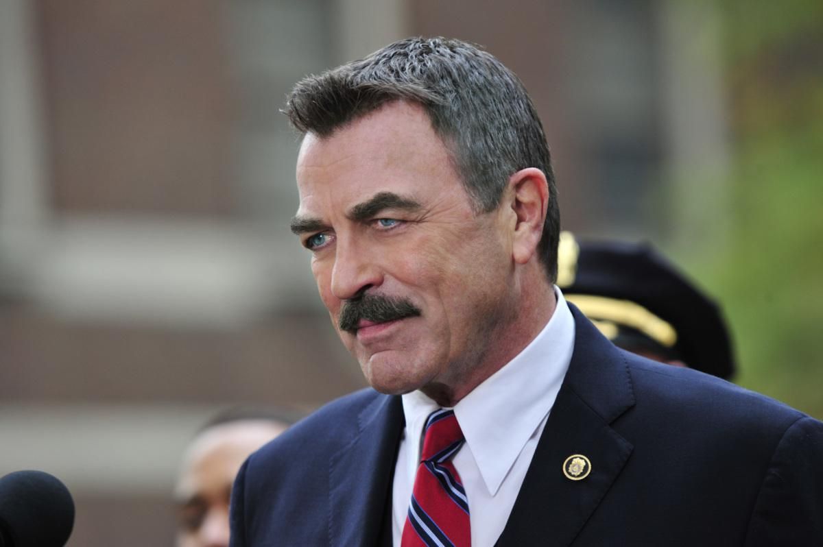 Tom Selleck as Frank Reagan in a navy blue suit and red striped tie