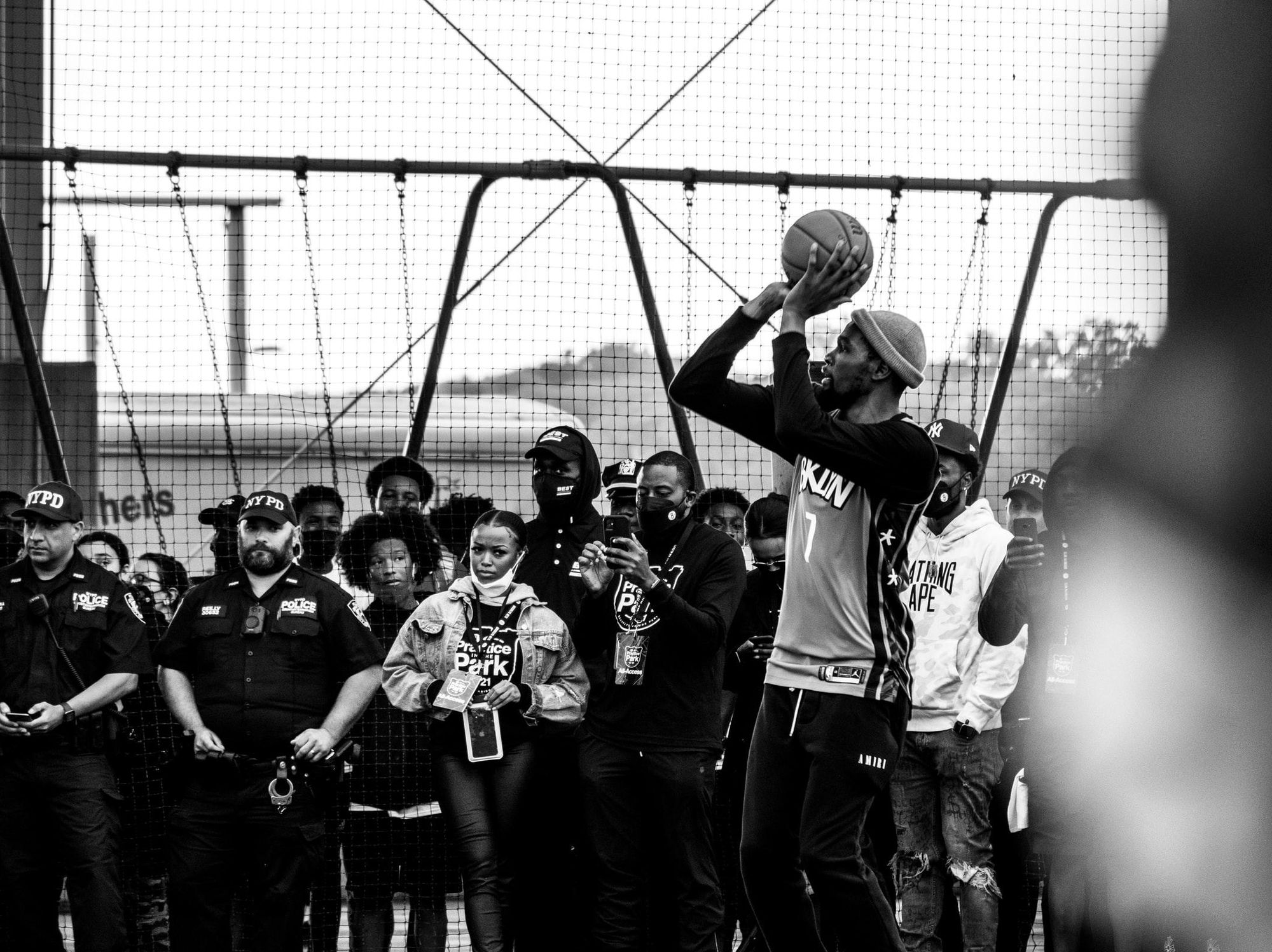 Kevin Durant holding a basketball in a shooting stance on a playground as spectators and NYPD officers look on