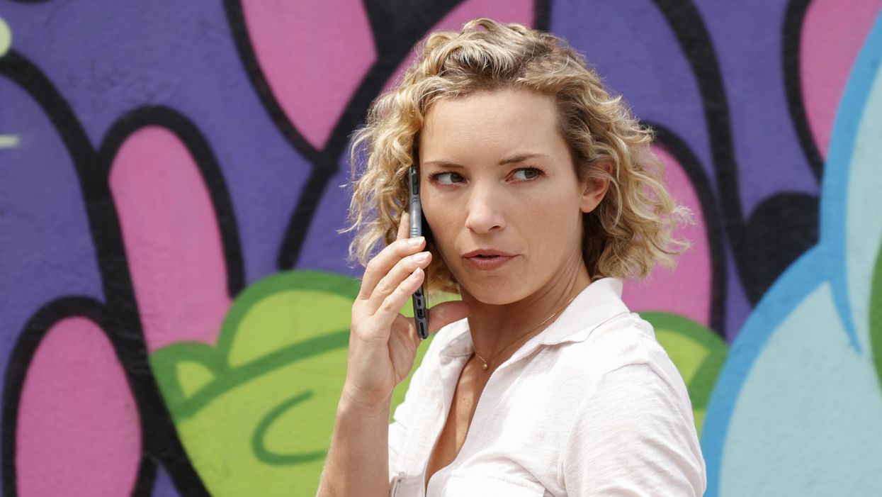 Perdita Weeks as Juliet Higgins holds a smartphone to her right ear in front of a colorful mural