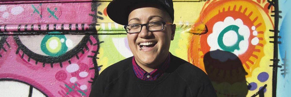 Picture of Gabby Rivera laughing in front of a colorful wall.