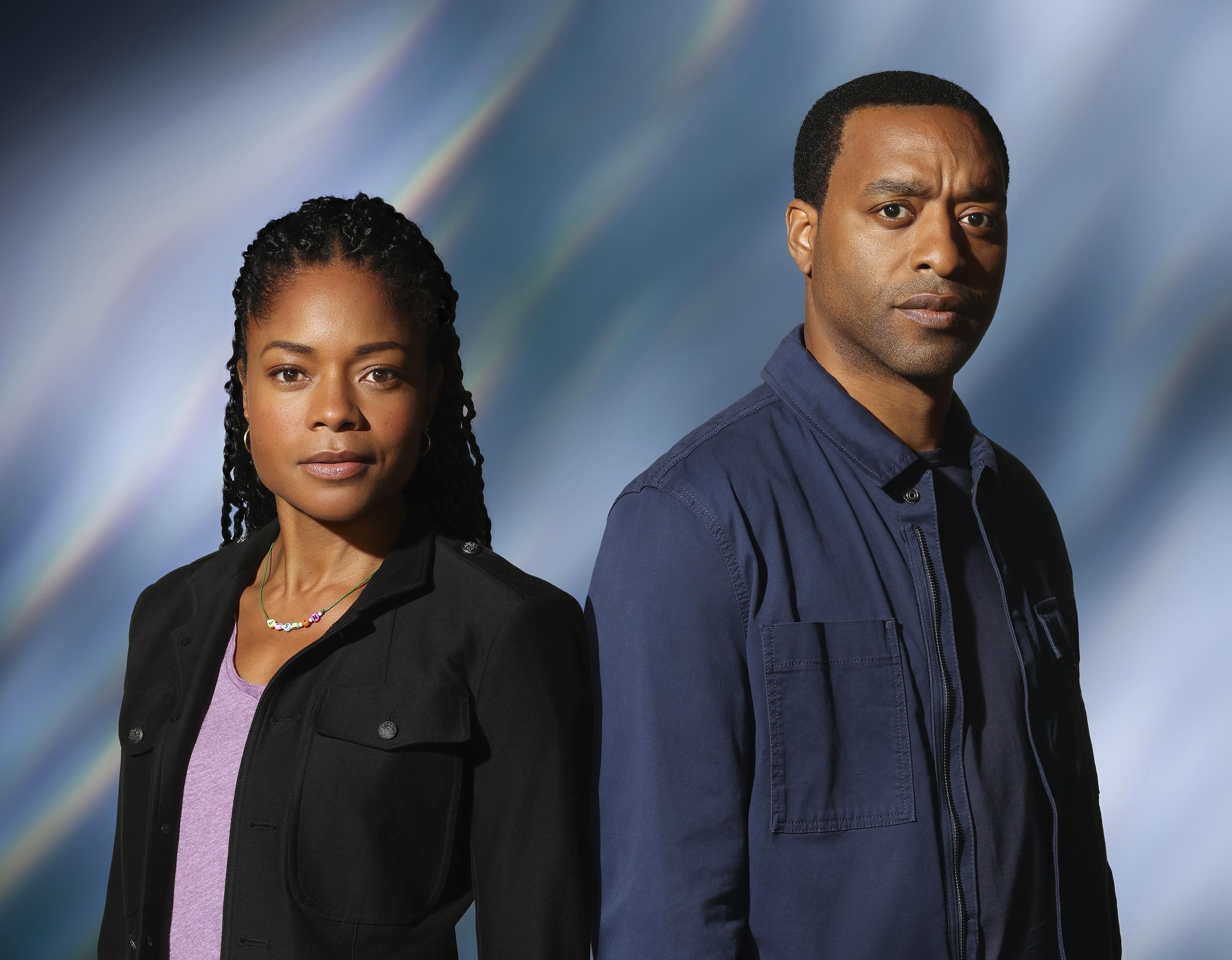 Actors Naomie Harris and Chiwetel Ejiofor stand in front a nebula backdrop dressed in their characters outfits