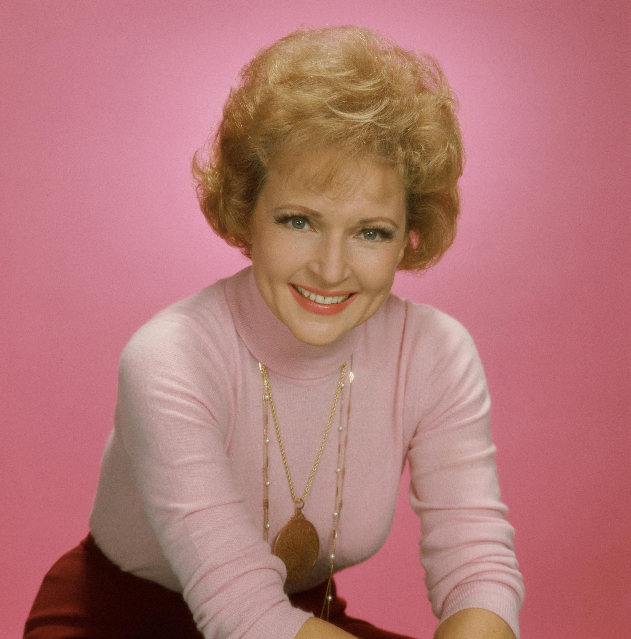 Actress Betty White in a pink and rose colored outfit against a pink backdrop in the 1970s