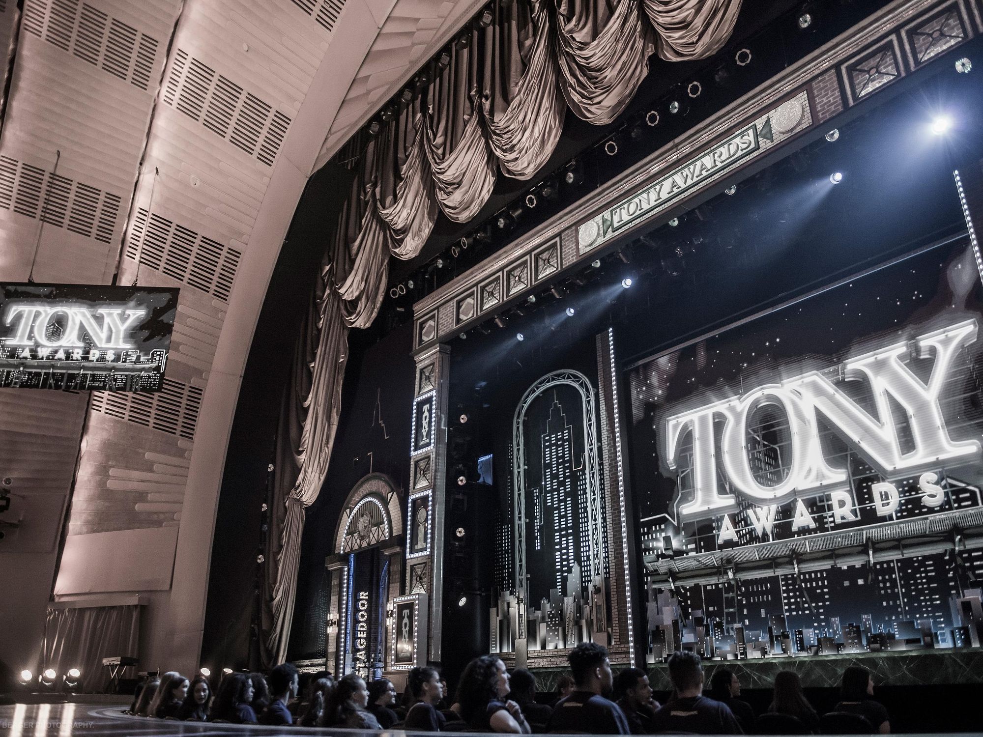 An audience level view of the Radio City Music Hall stage with the words Tony Awards in white lights and an outline of the NYC skyline behind them
