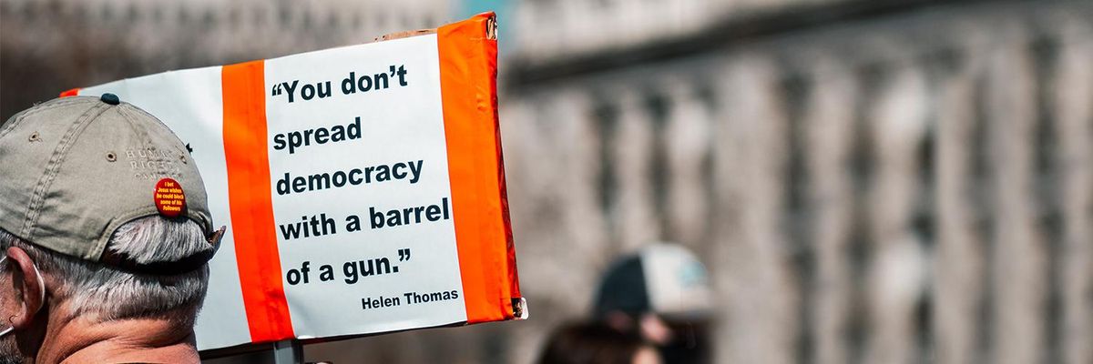 Pictured: man in a protest holding up a sign that says: You don't spread democracy with a barrel of a gun- Helen Thomas