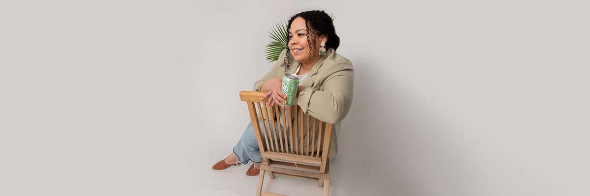 woman sits on chair looking away from the camera with a canned beverage in her hand 
