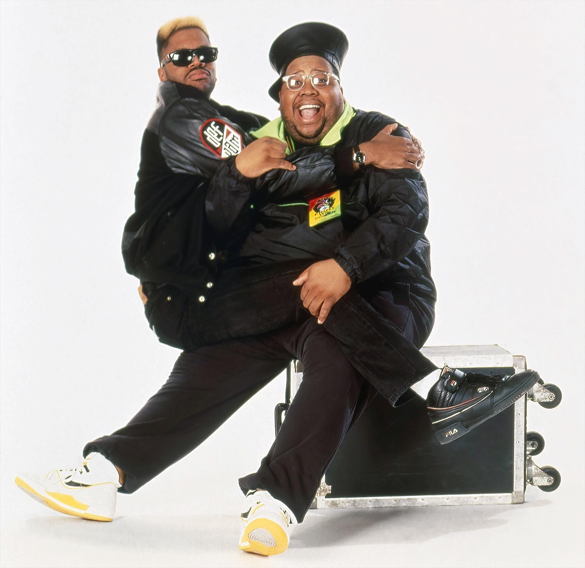 Yo! MTV Raps hosts Ed Lover and Doctor Dre wearing black jackets and pants with sneakers and goofing around on the set