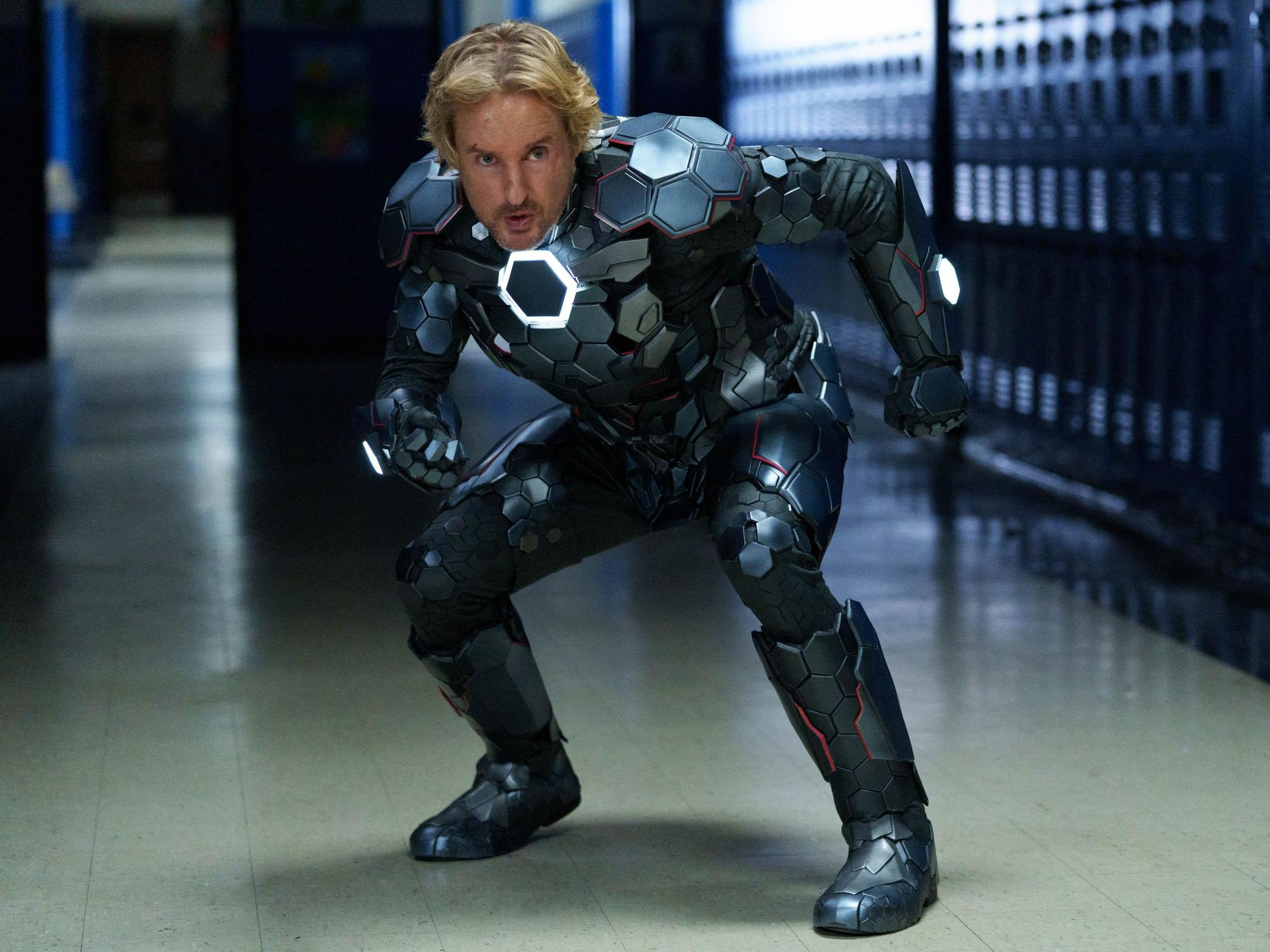 Owen Wilson as Jack standing in a school hallway in a metal superhero costume