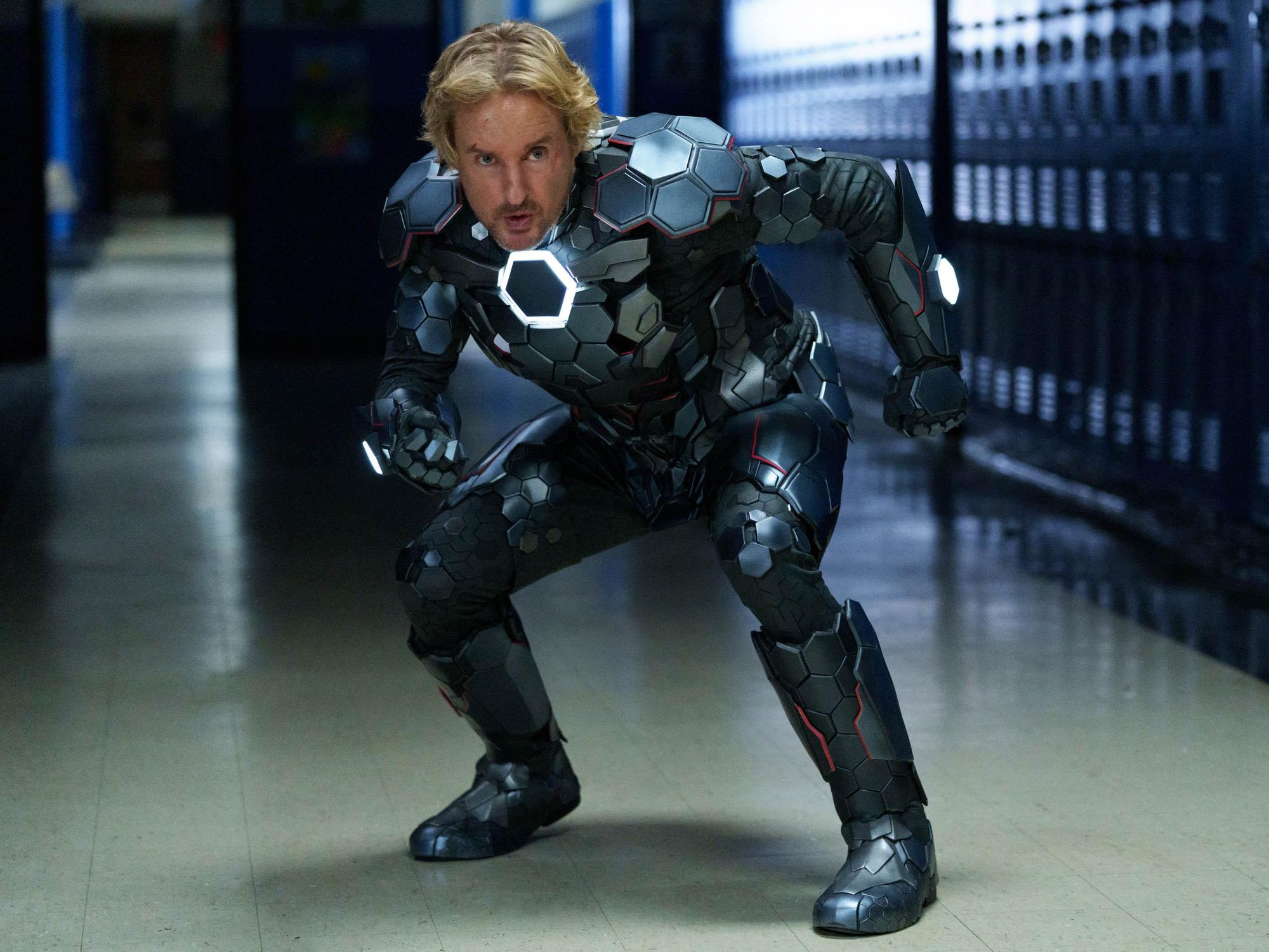 Owen Wilson as Jack standing in a school hallway in a metal superhero costume