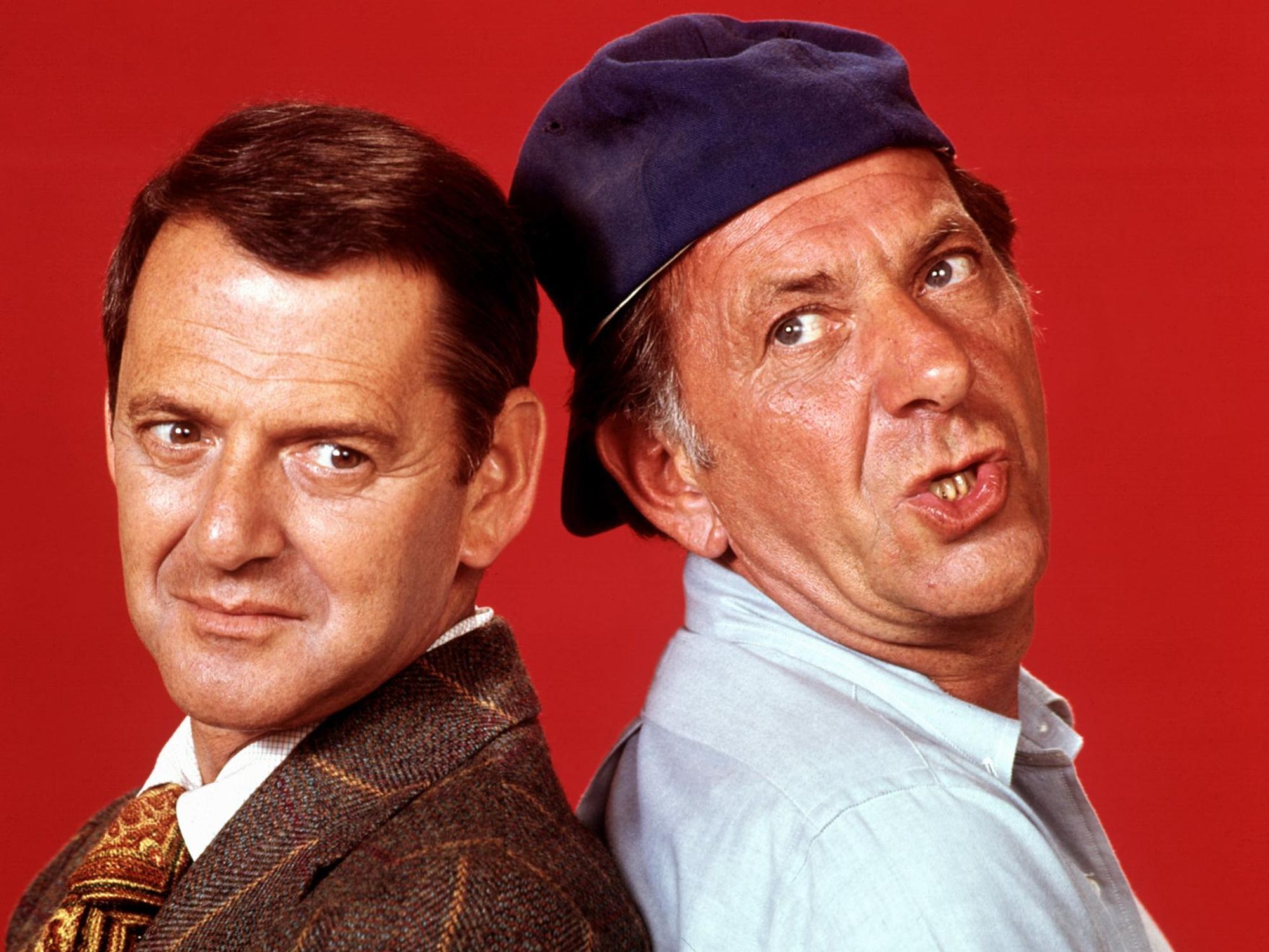 Oscar and Felix from the TV classic The Odd Couple stand back to back against a crimson backdrop.