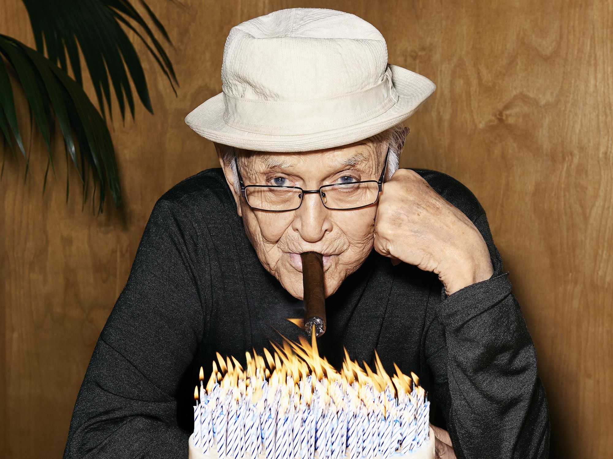 Prolific producer Norman Lear sits with a cigar poised over a birthday cake with 100 candles blazing away.