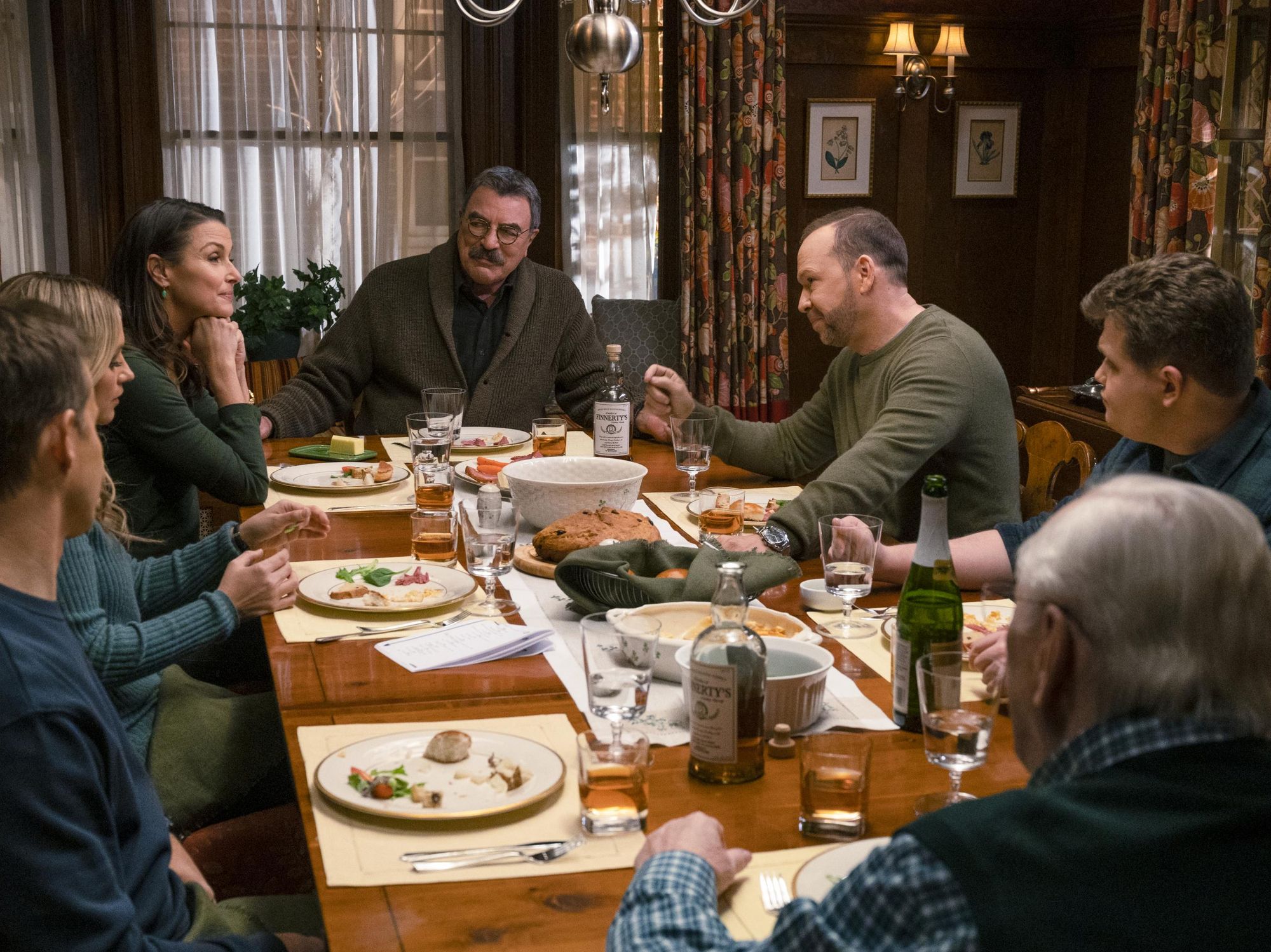 Frank Reagan sits at the head of the dinner table next to Erin and Danny surrounded by the rest of his family after a meal. 