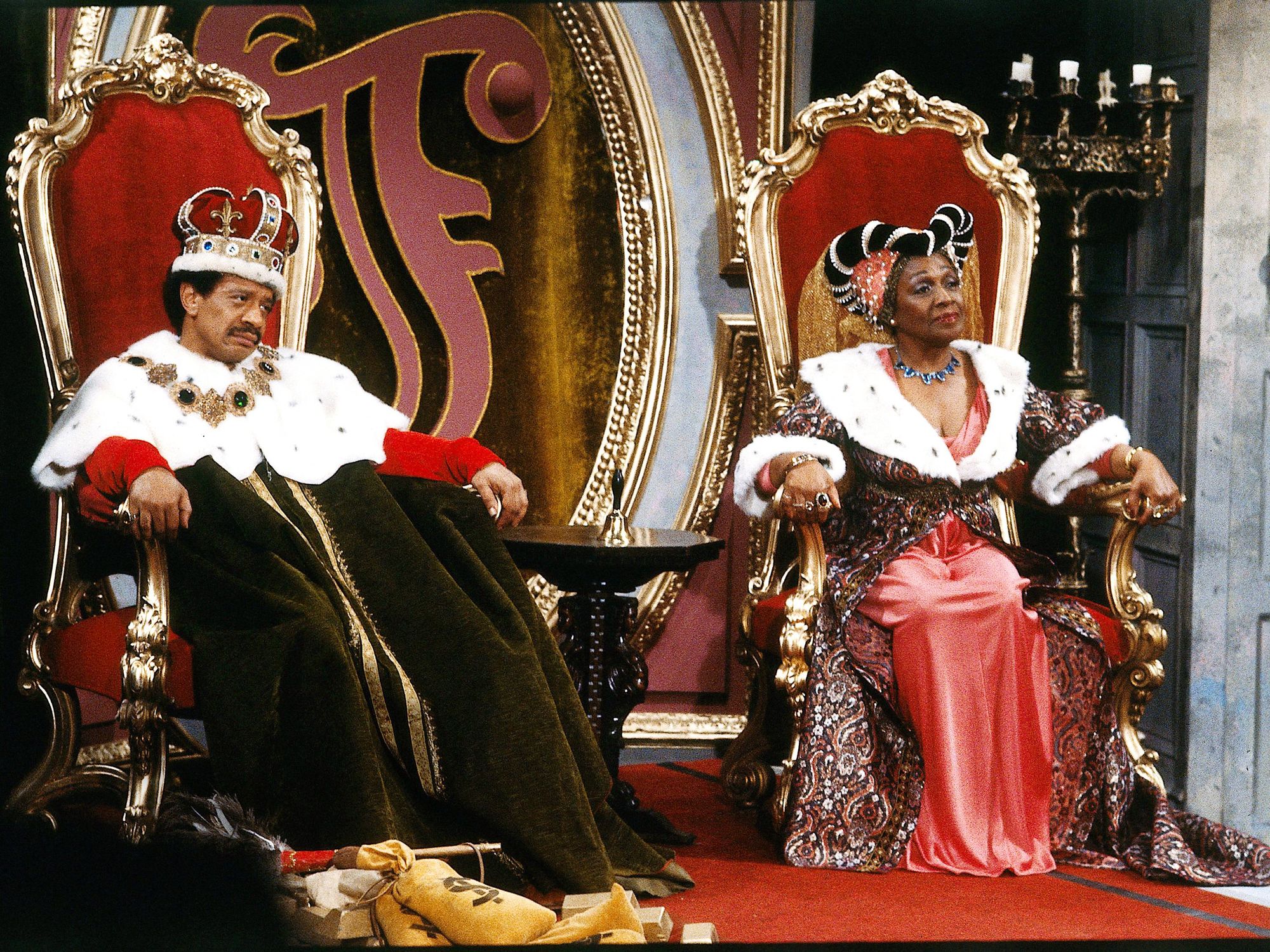 George and Louise Jefferson sit on royal thrones while wearing crowns and regal attire.
