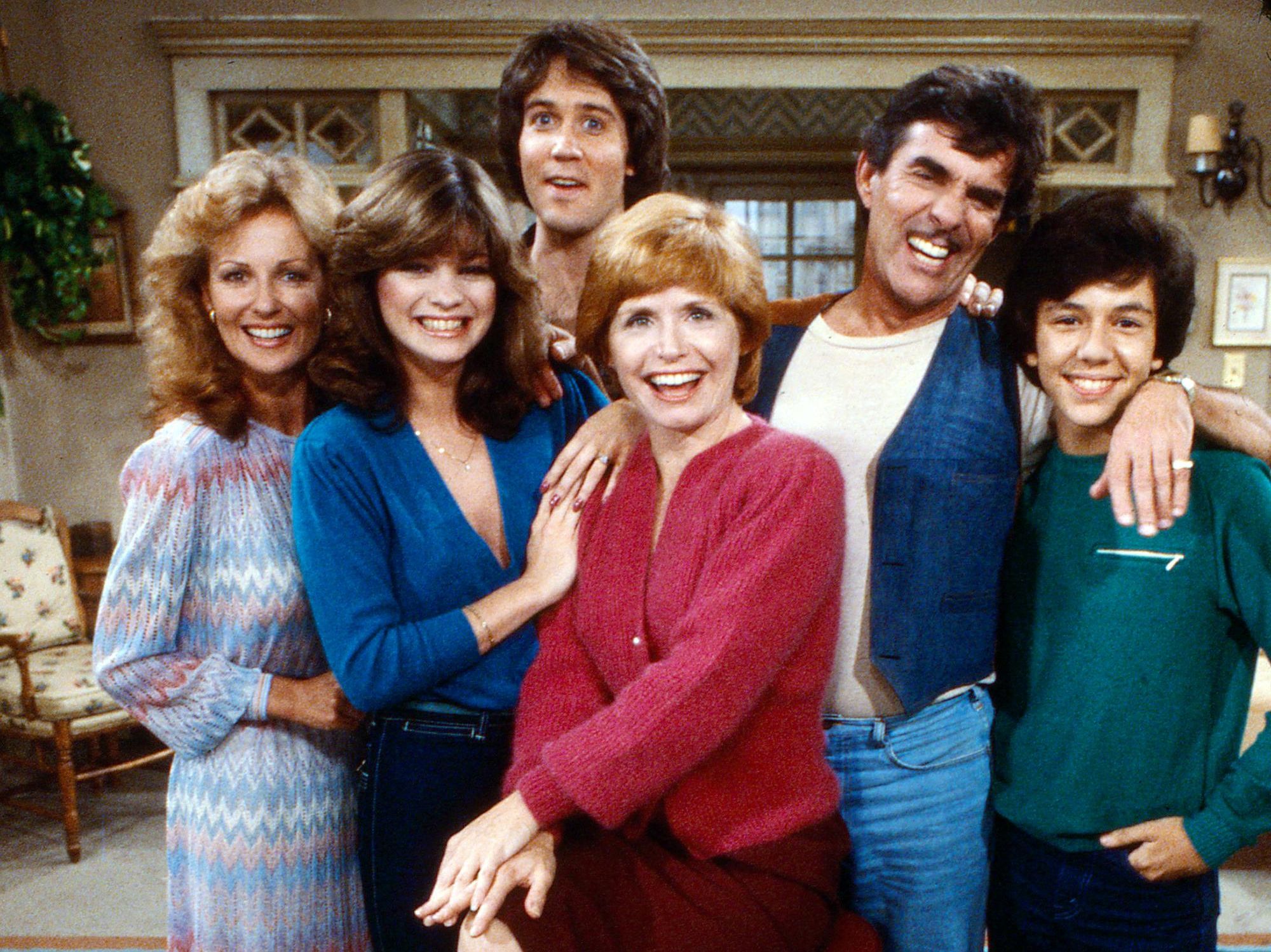 The Cast of One Day at a Time smiles and poses on the living room set of the show.