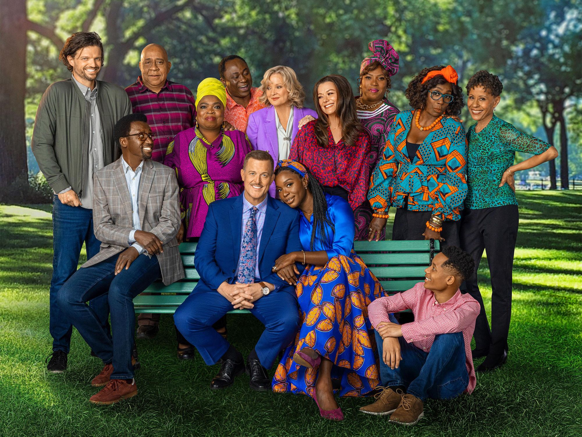 The cast of Bob Hearts Abishola surrounds the two stars of the show as they sit together on their favorite park bench.